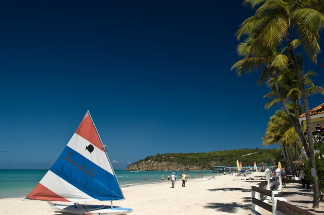 A small sailboat and palm trees on Dickenson Bay beach, Antigua.