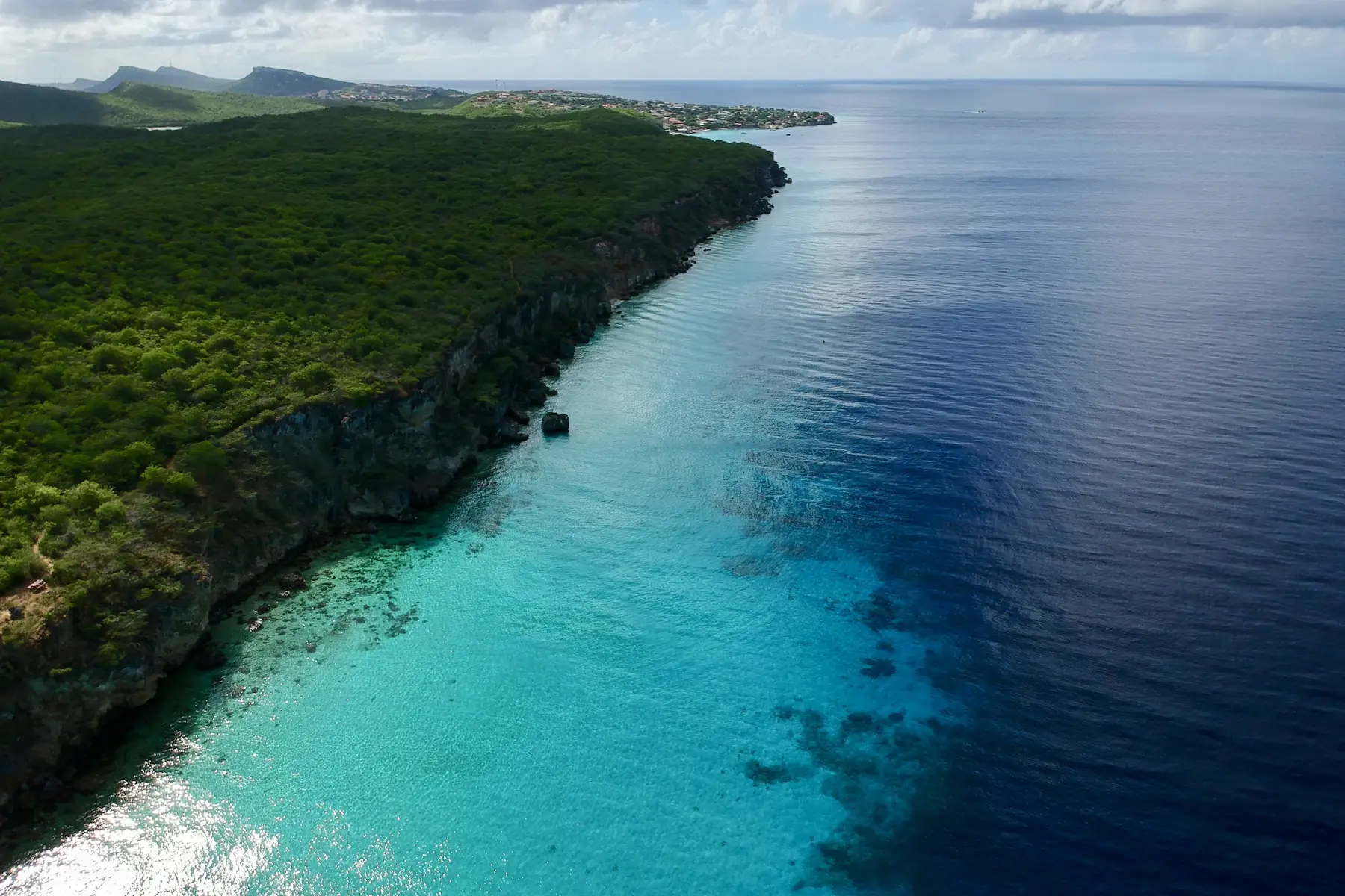 Green coastal cliffs and clouds above the sea near Kokomo, Curaçao